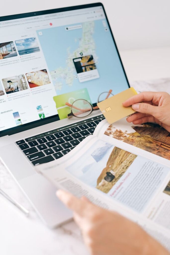 pexels-photo-8937451 Hands holding credit card over laptop and magazine for online shopping and travel planning.